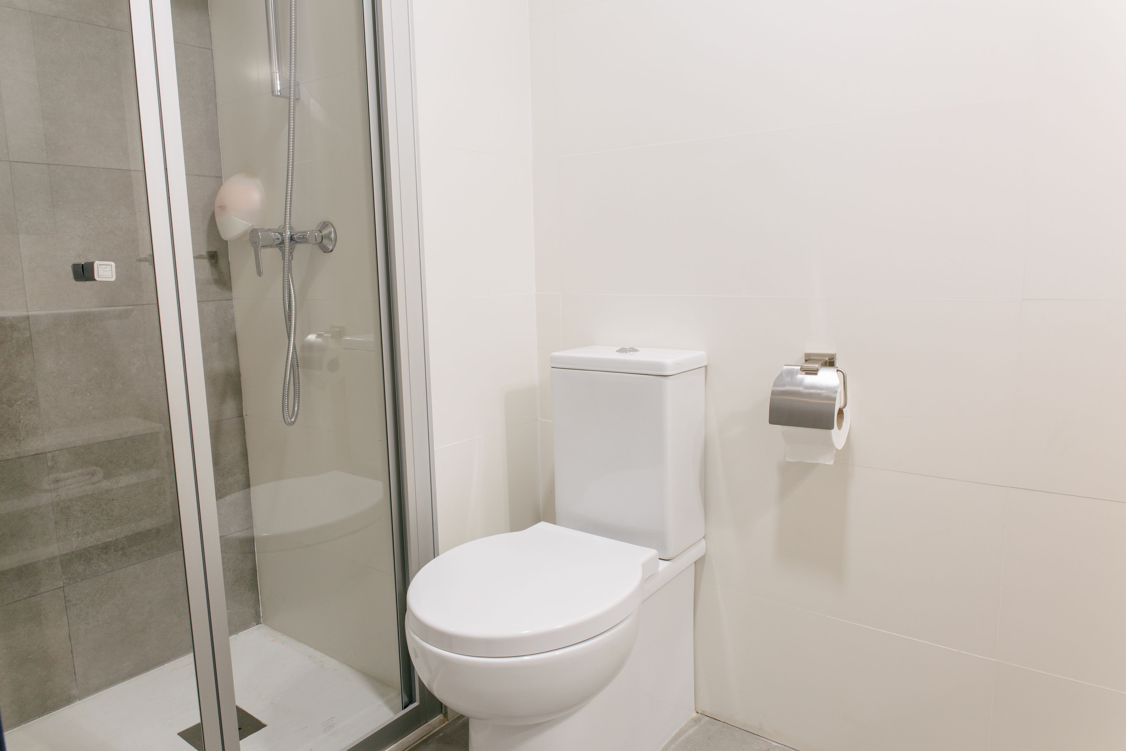 A bathroom with a glass-enclosed shower, a white toilet, and a paper towel dispenser.
