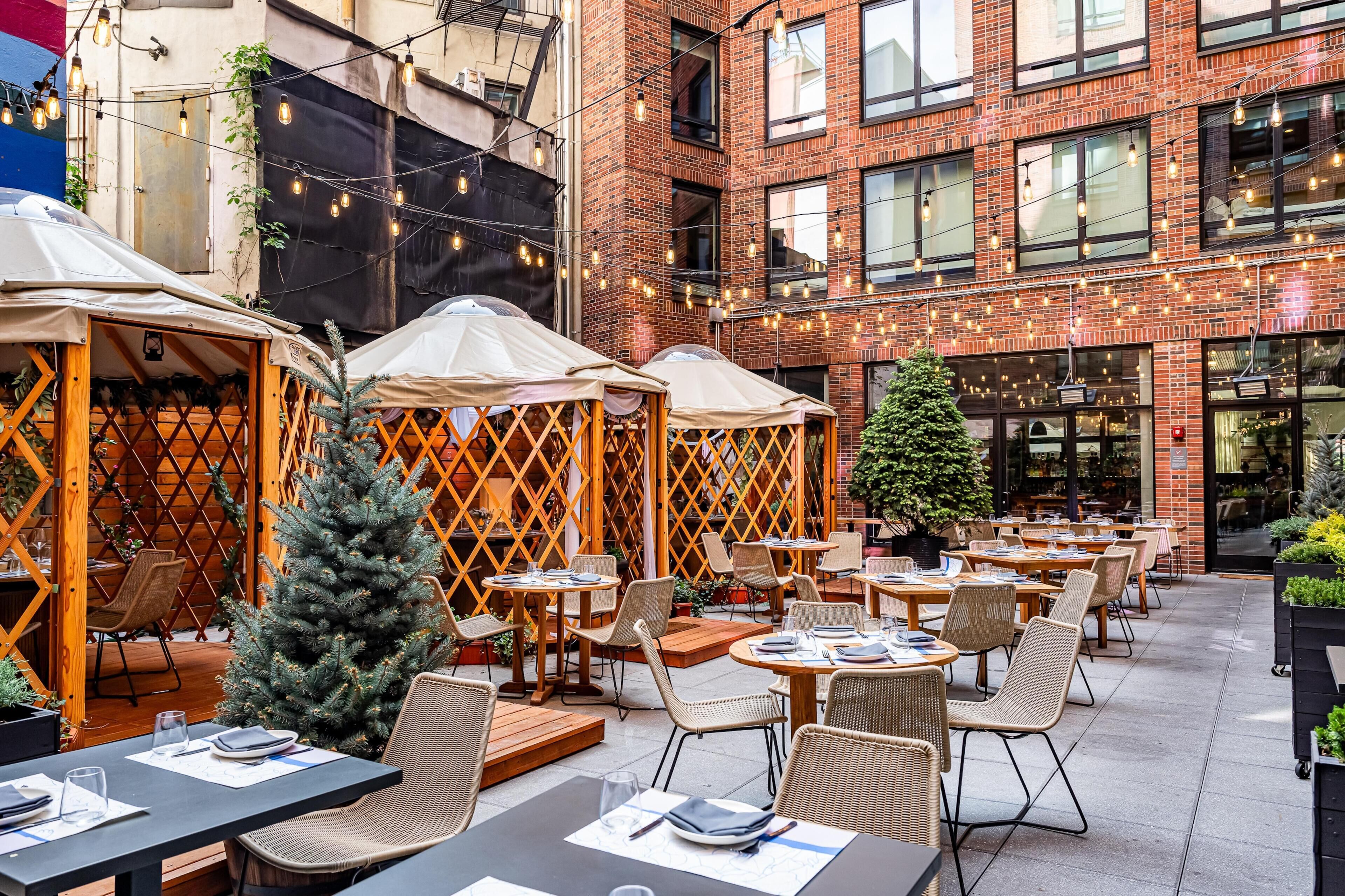 An outdoor café with tables and chairs, a Christmas tree, and string lights.