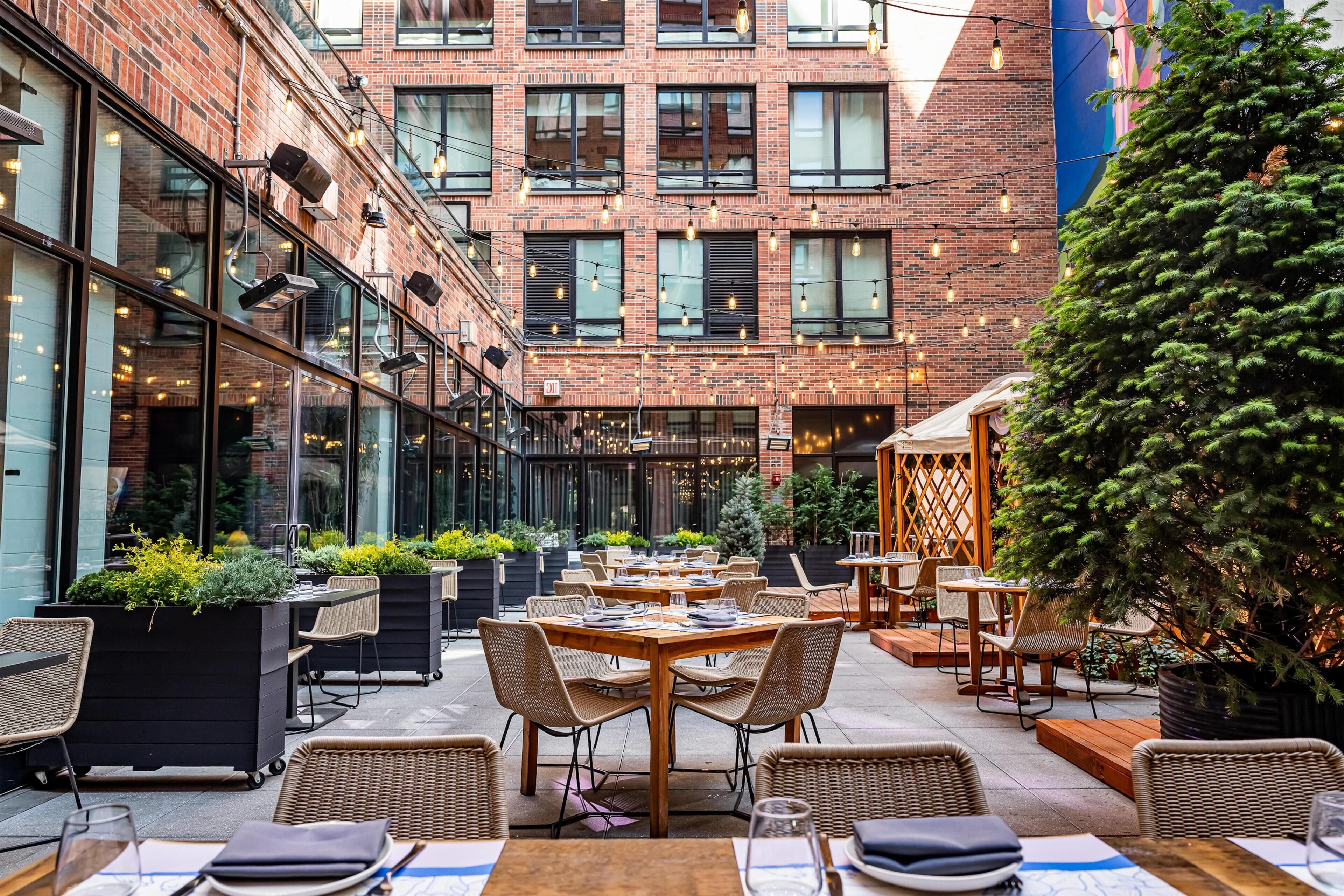 An outdoor dining area with brick buildings, tables, chairs, and potted plants.
