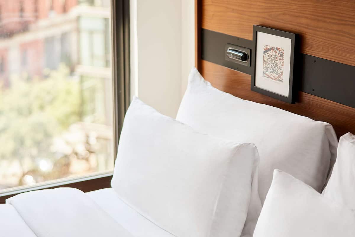 A neatly made bed with white linens and pillows, a wooden headboard, and a framed picture on the wall.