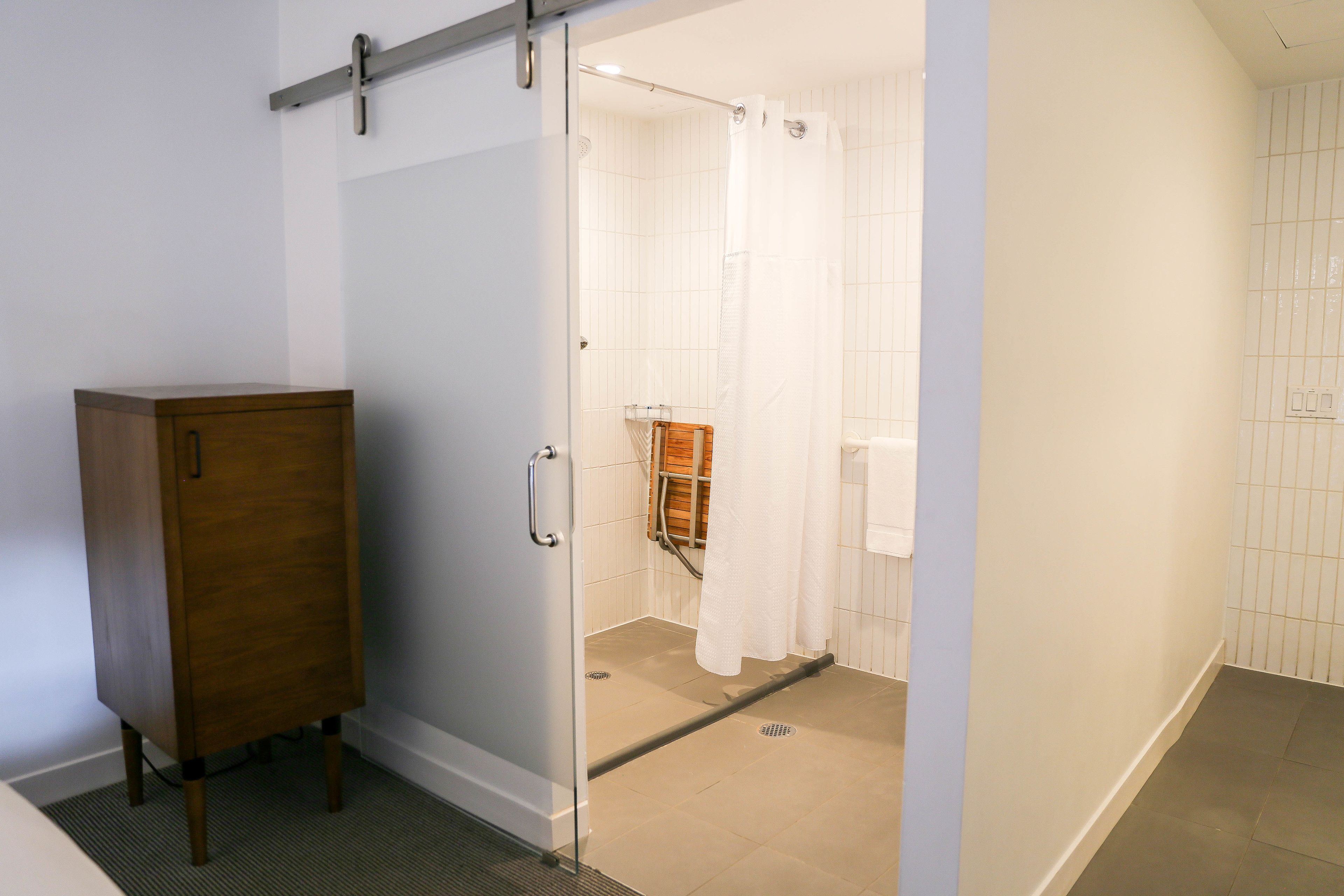 A bathroom with a glass shower enclosure, a wooden cabinet, and white tiled walls.