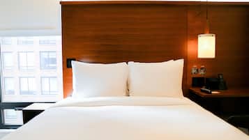 Habitación de hotel con una cama grande, cabecero de madera, mesita de noche con lámpara y vistas a edificios a través de la ventana.