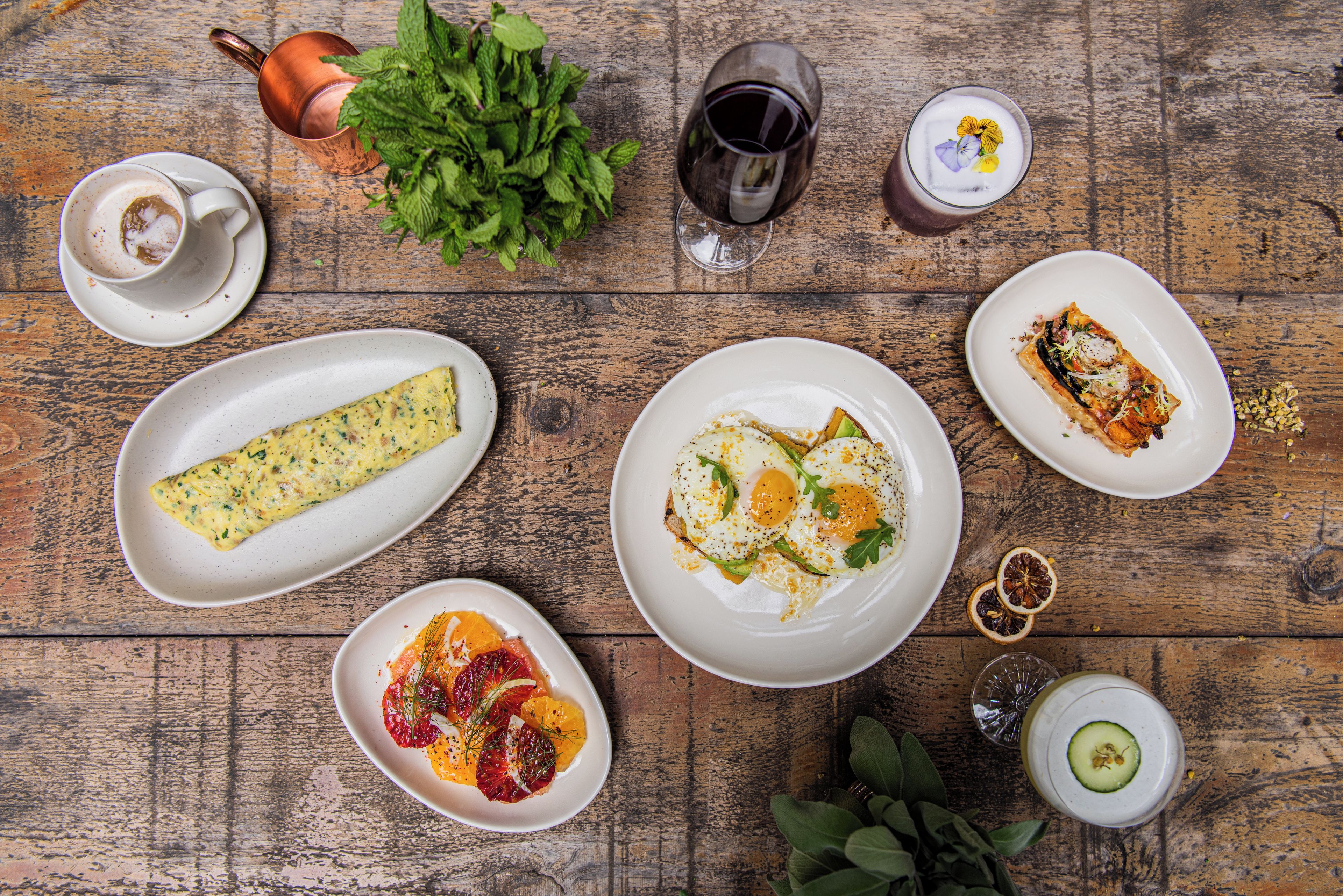 A wooden table with various dishes including an omelette, a citrus salad, and a plate with a rolled omelette.