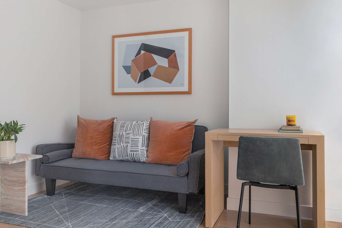 A modern living room with a grey sofa, a small wooden table, and a framed abstract painting on the wall.