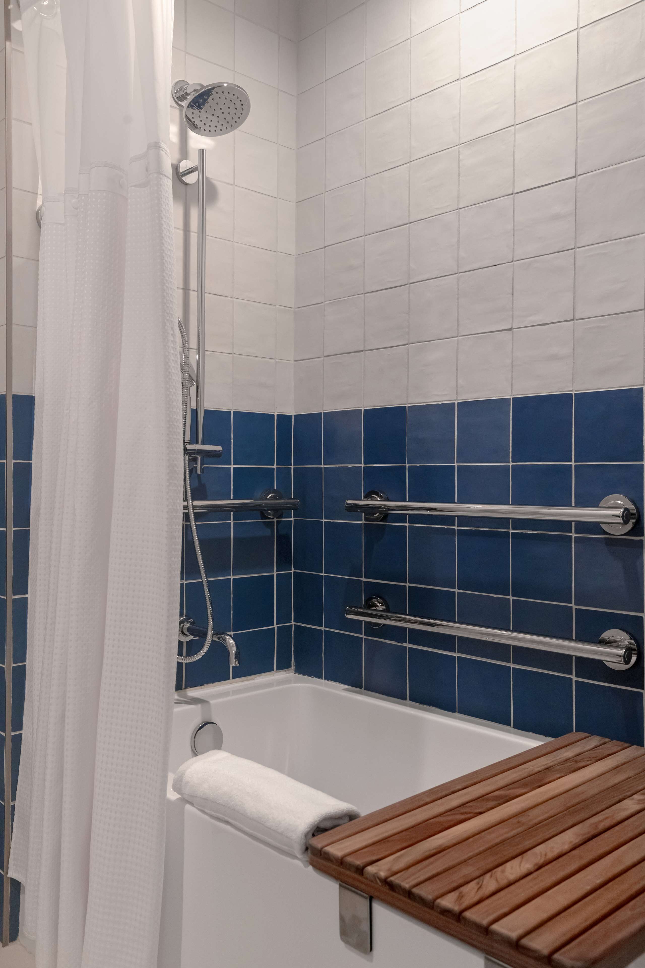 Zona de ducha con cabezal, toallero y banco de madera.