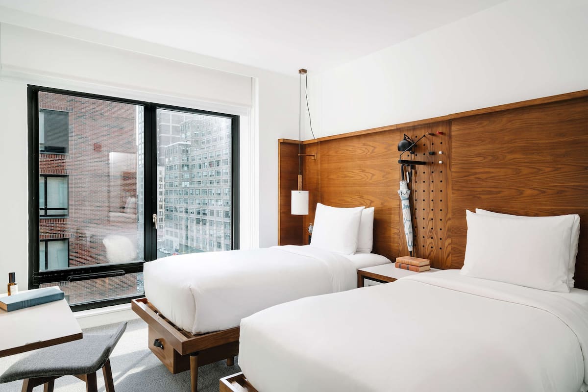 A hotel room with two beds, a desk, and a chair.