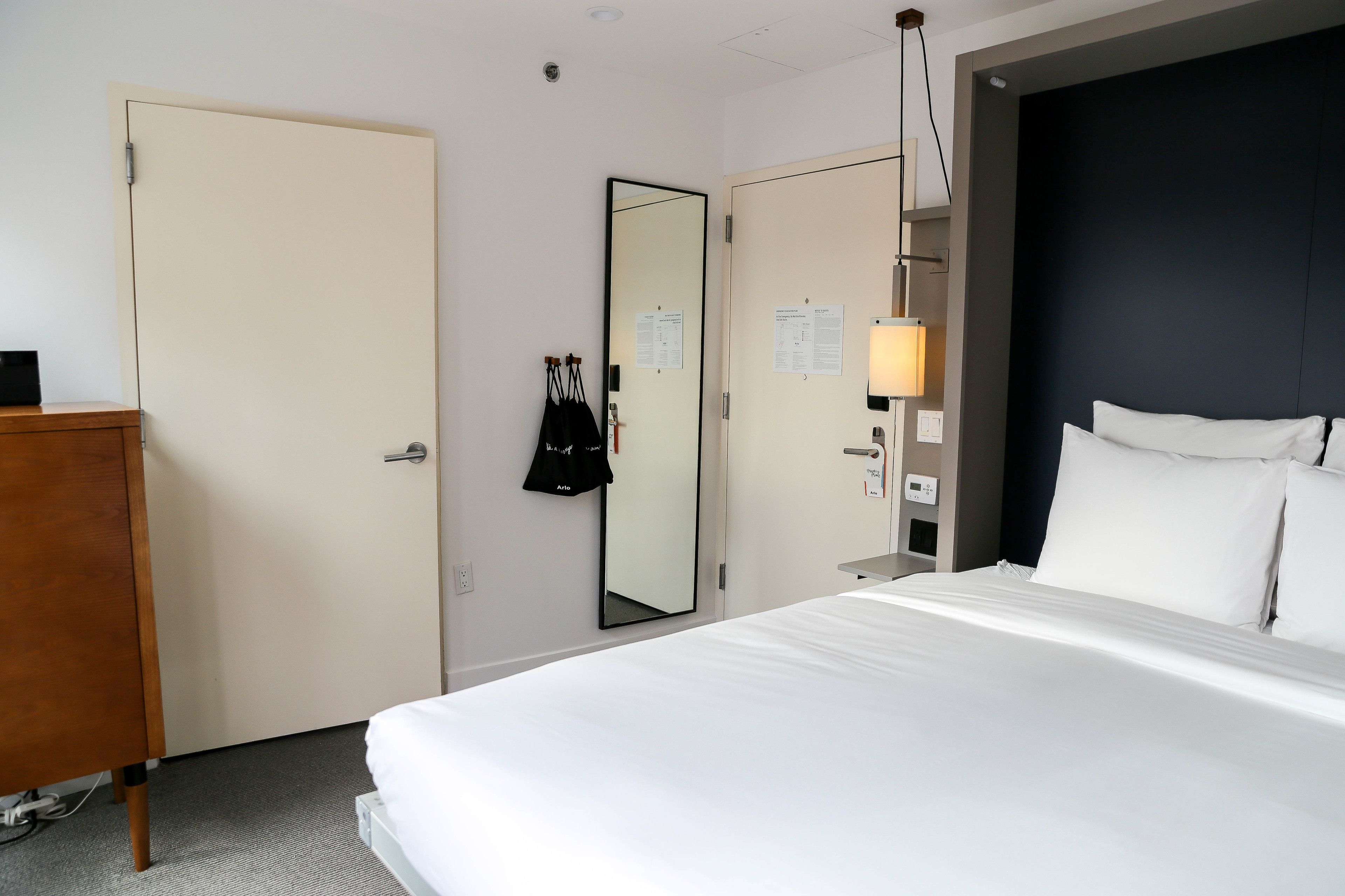 Una habitación de hotel con cama, armario, espejo y escritorio con lámpara.