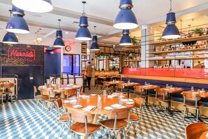 A restaurant with blue pendant lights, checkered floor tiles, and a neon sign reading "Harrods".
