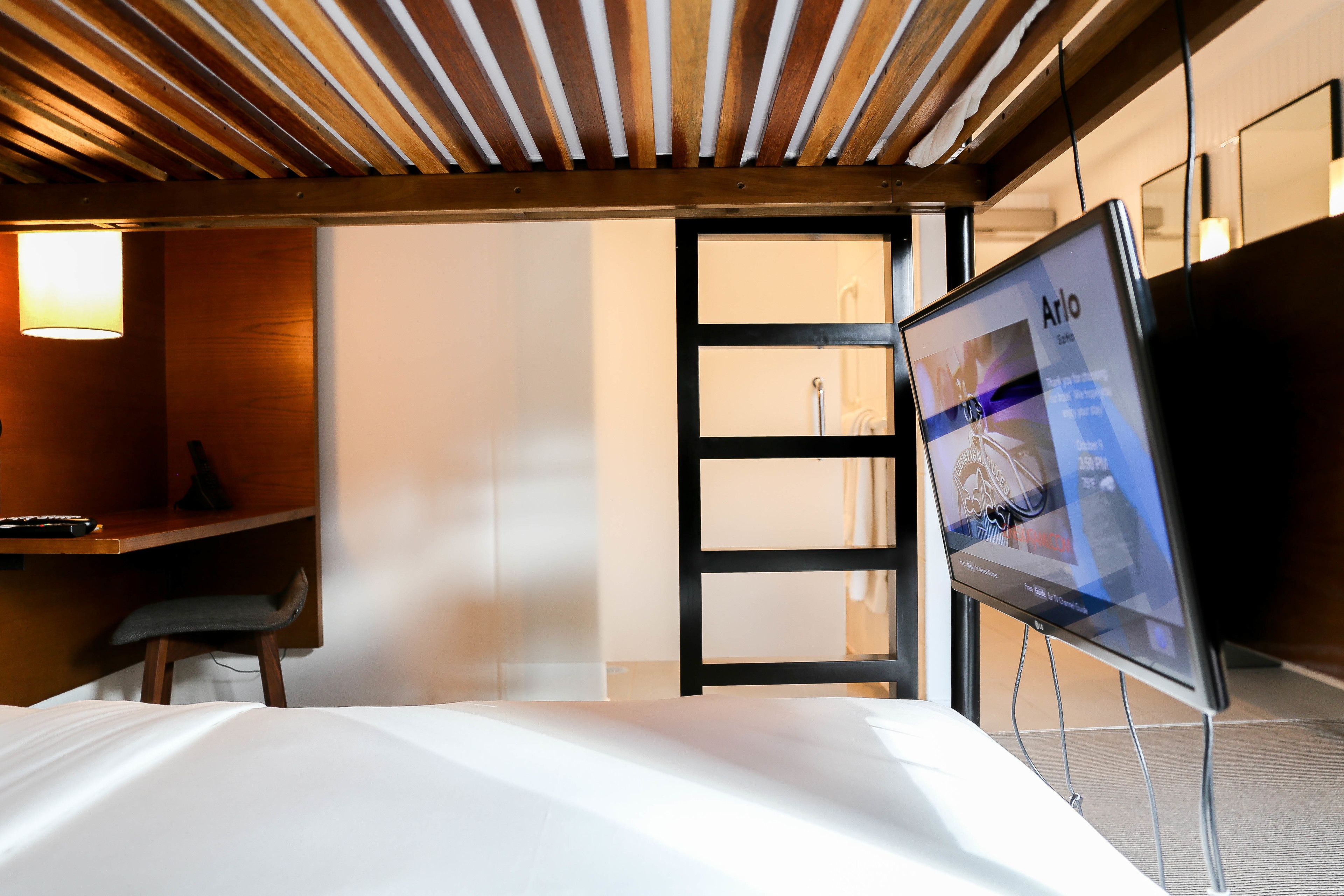 A hotel room with a bed, a desk, and a TV displaying 'Arlo' on the screen.