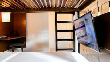 A hotel room with a bed, a desk, and a TV displaying 'Arlo' on the screen.