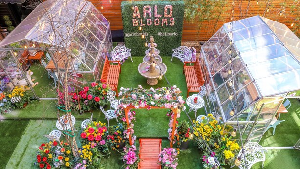 A greenhouse with a floral archway, seating areas, and a sign reading "ARLO BLOOMS". - Arlo SoHo (New York)