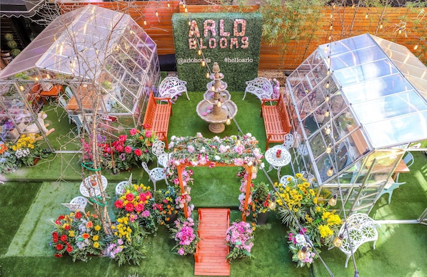 A greenhouse with a floral archway, seating areas, and a sign reading "ARLO BLOOMS".