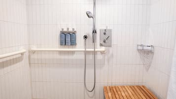A shower area with white tiled walls, a wooden bench, a handheld showerhead, and a soap dispenser on a shelf.