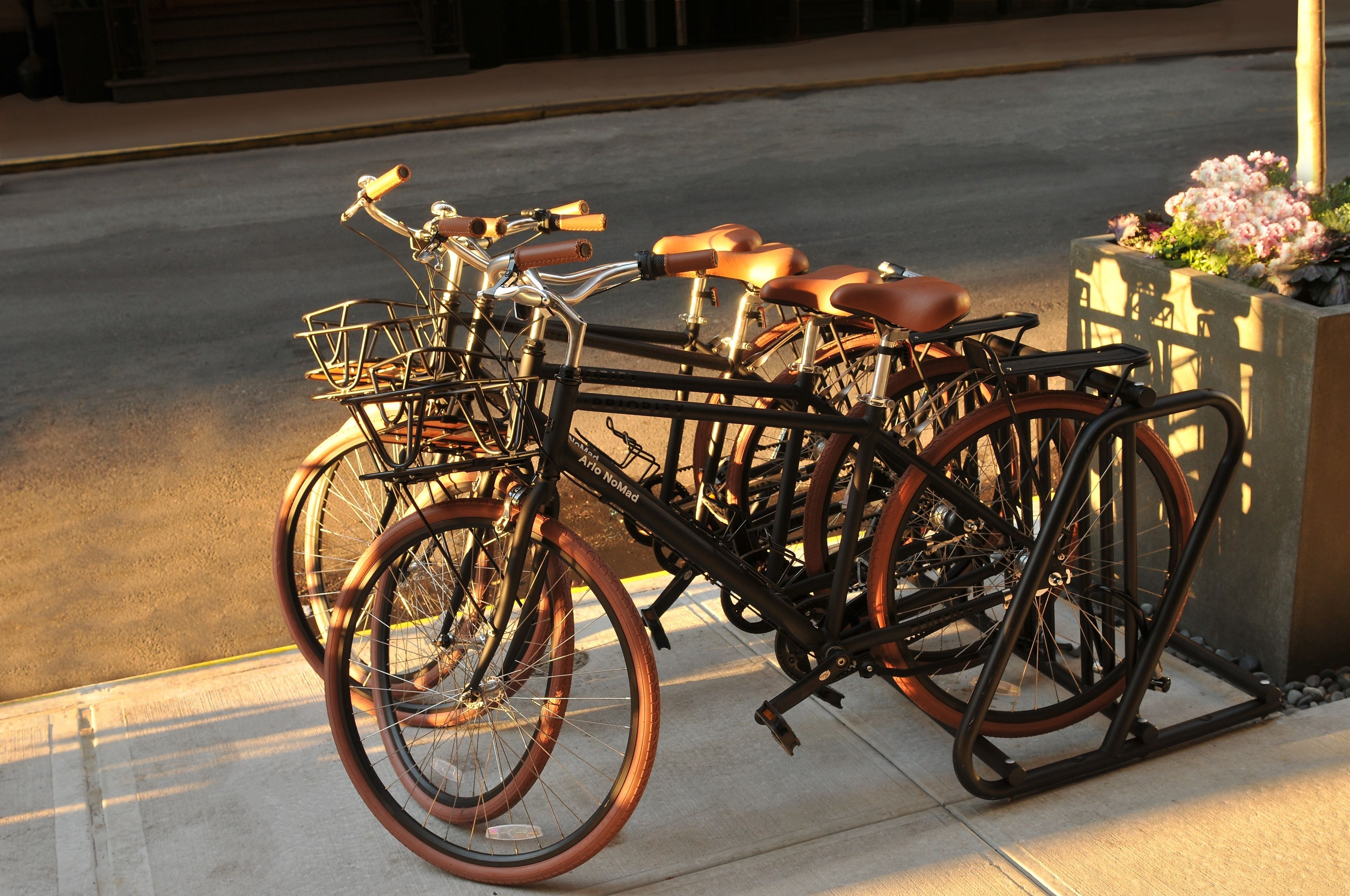 A stationary bicycle with a basket and leather seats parked on a sidewalk.