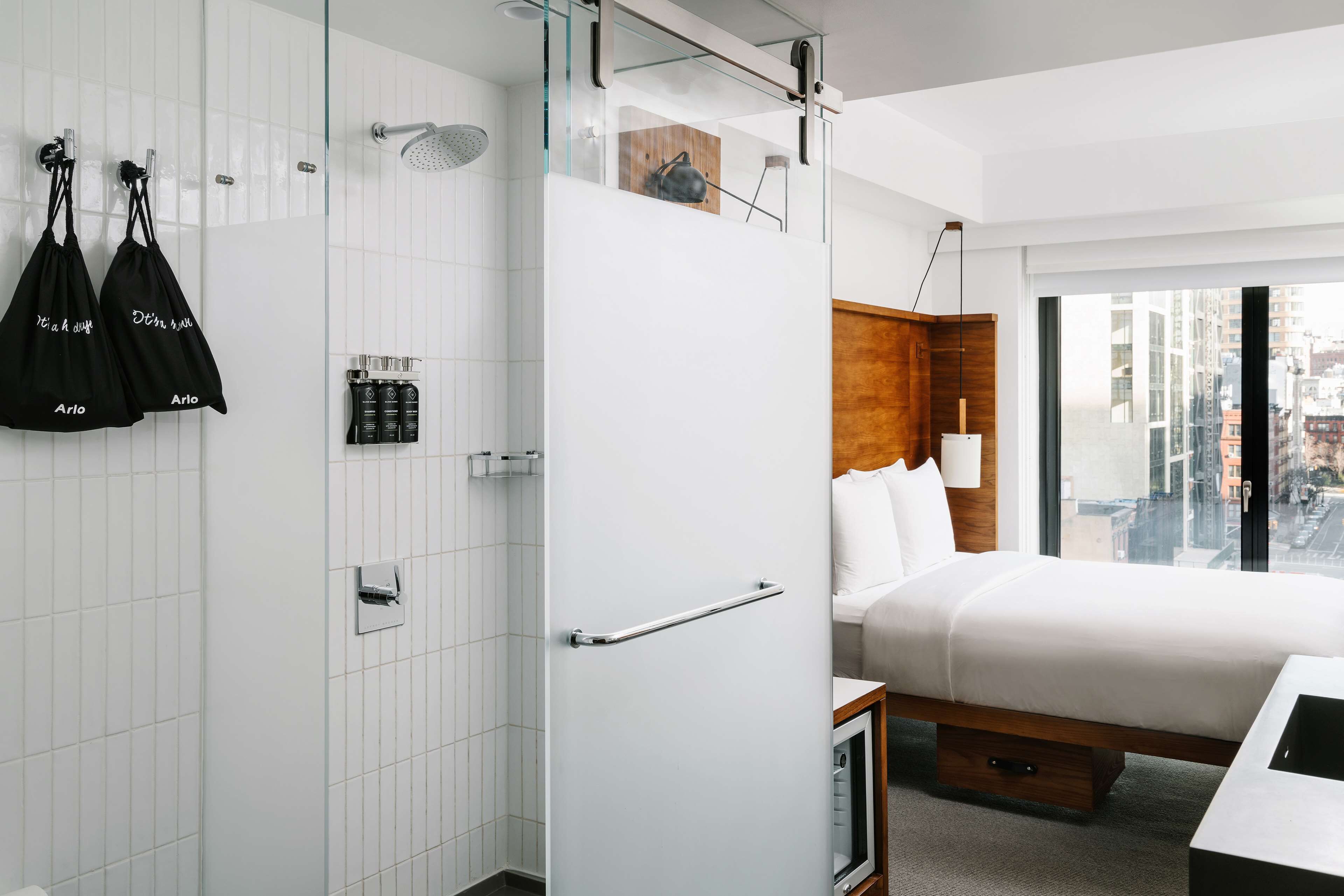 A modern hotel room with a bed, bedside table, and a view of the city.