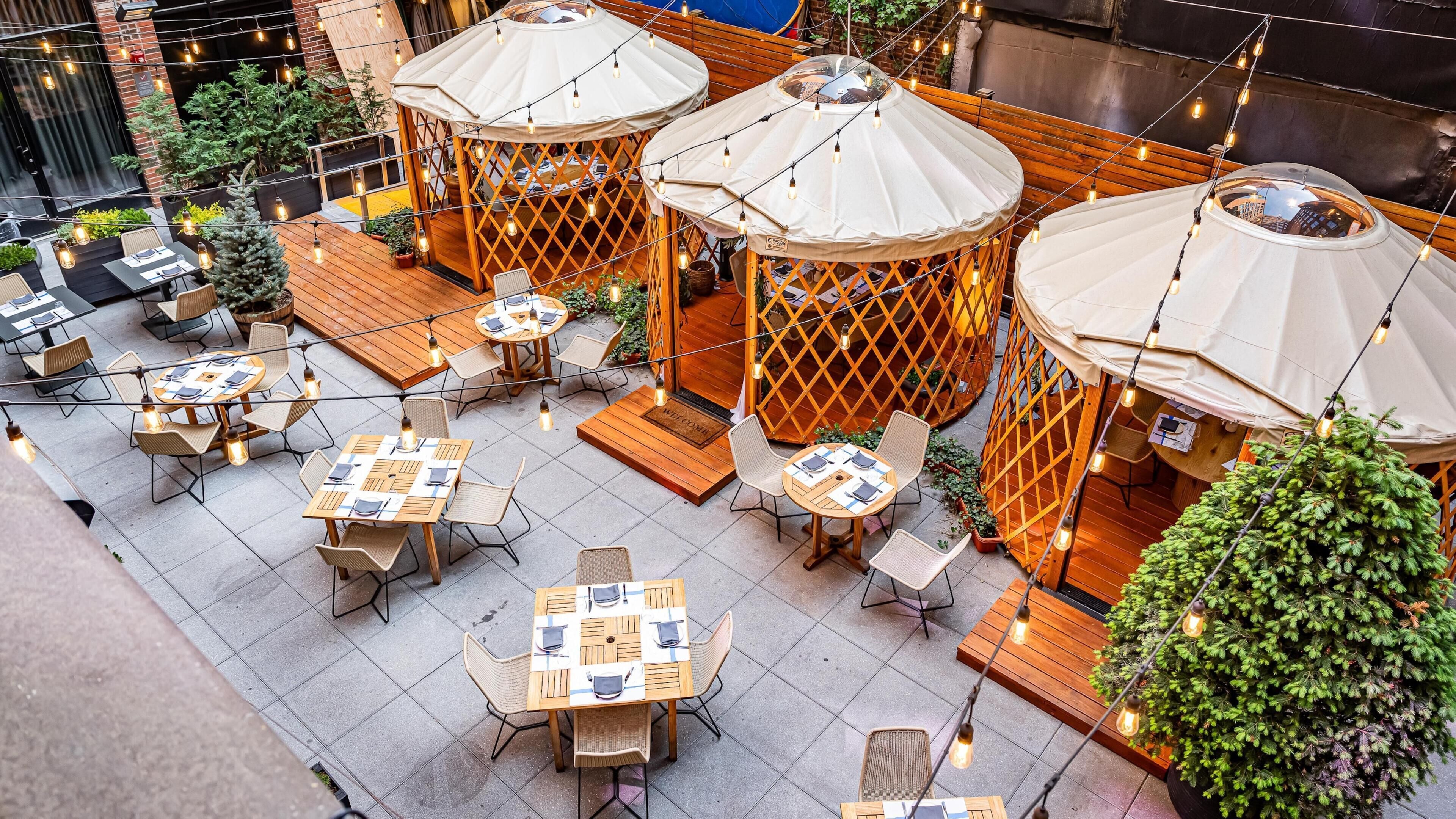 An outdoor seating area with tables and chairs, covered by umbrellas, and string lights.