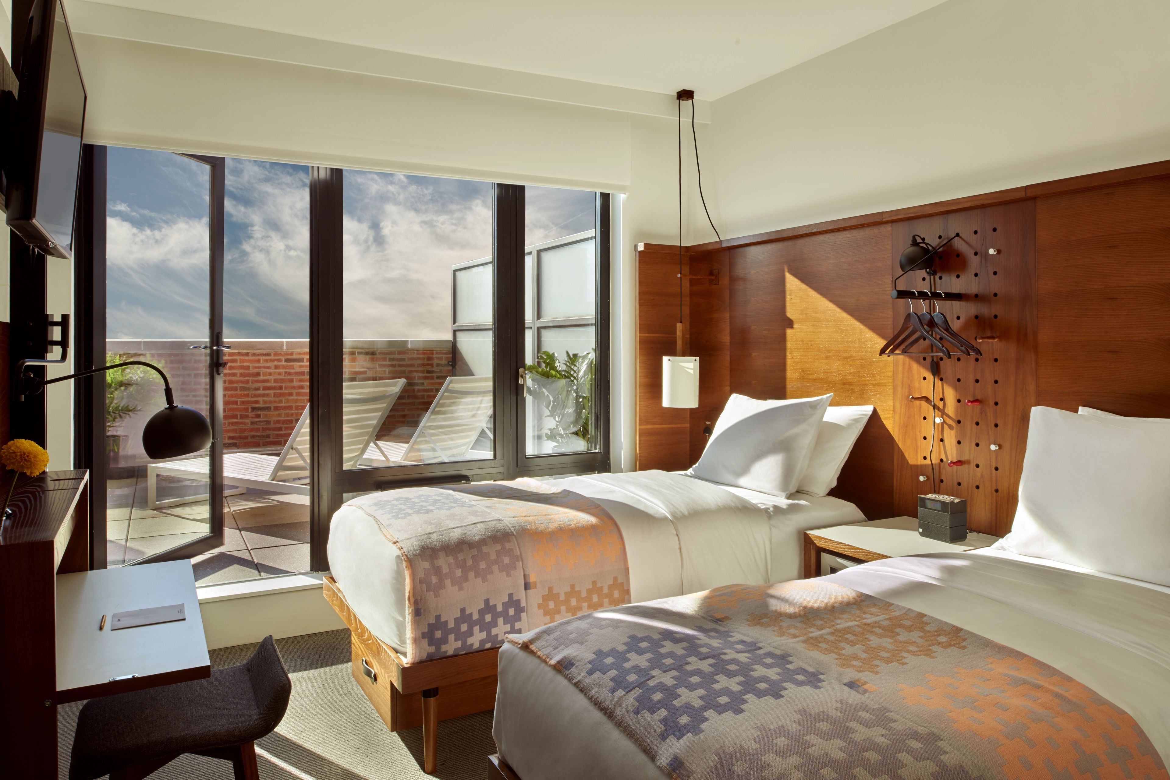 A hotel room with two beds, a desk, and a large sliding glass door leading to a balcony.