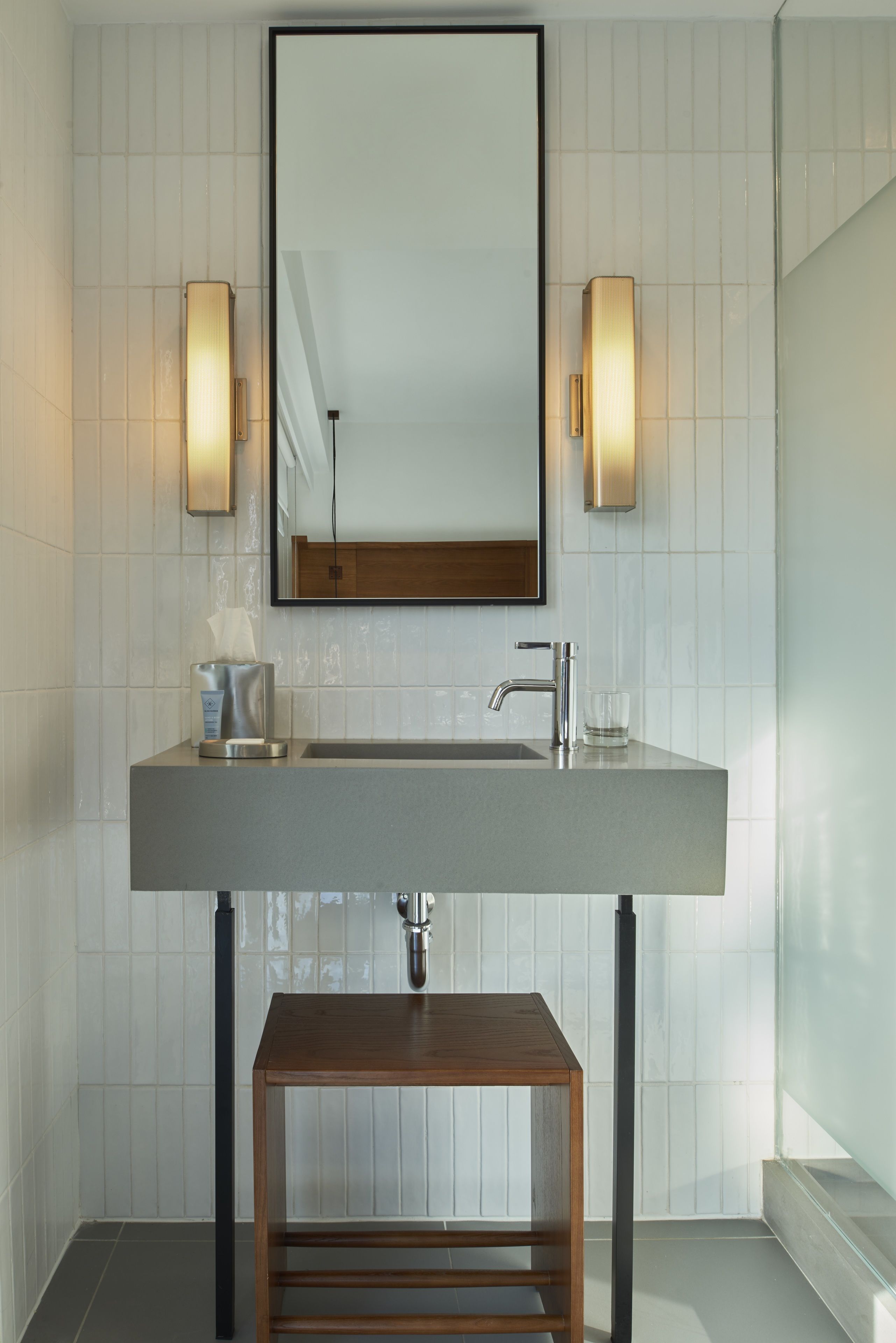 A modern bathroom with a large rectangular sink, two wall-mounted lights, a mirror, and a wooden bench.