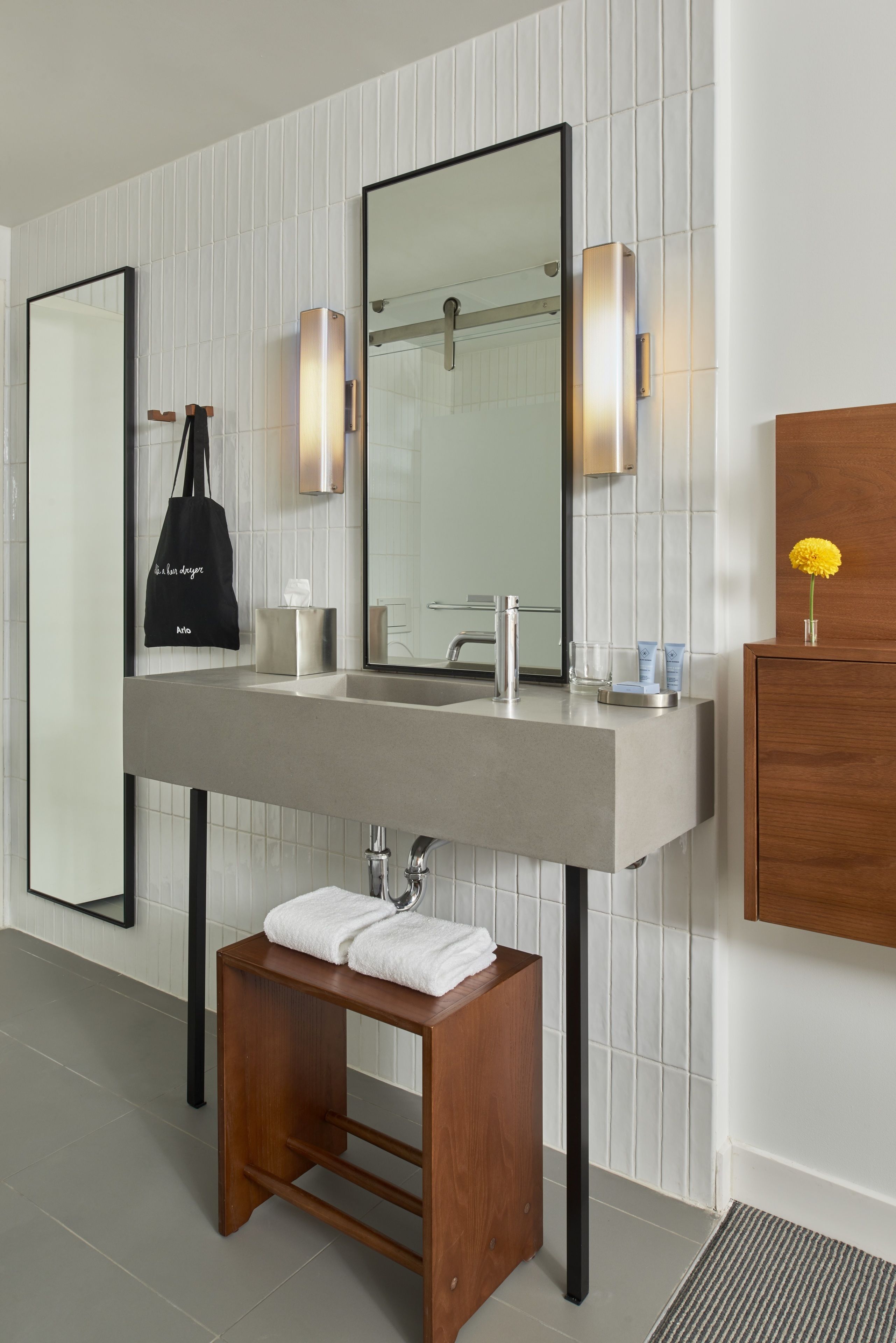 A modern bathroom with a large mirror, a wooden stool, and a towel rack.