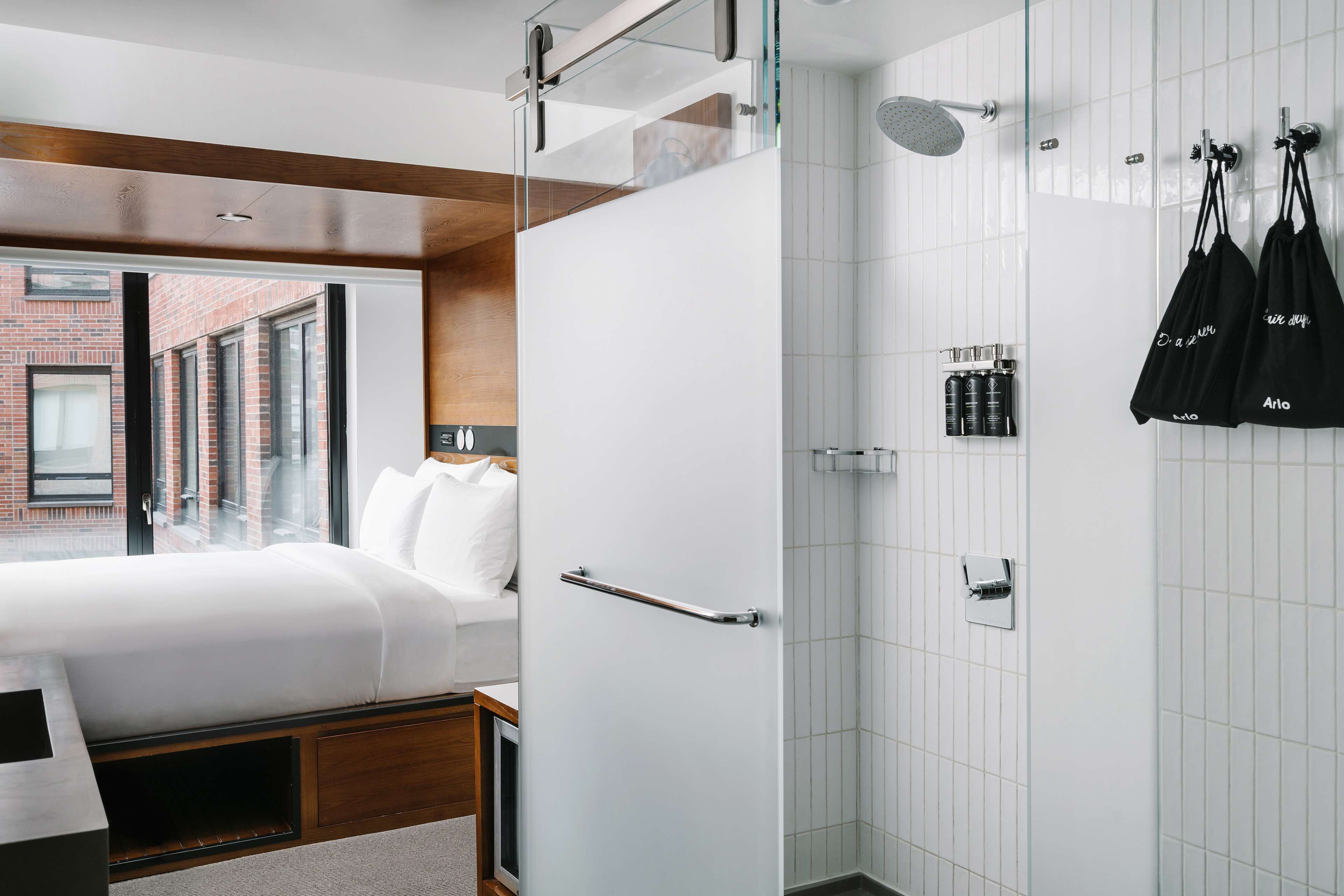 A modern hotel room with a bed, a shower, and a view of a brick building.
