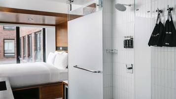 A modern hotel room with a bed, a shower, and a view of a brick building.