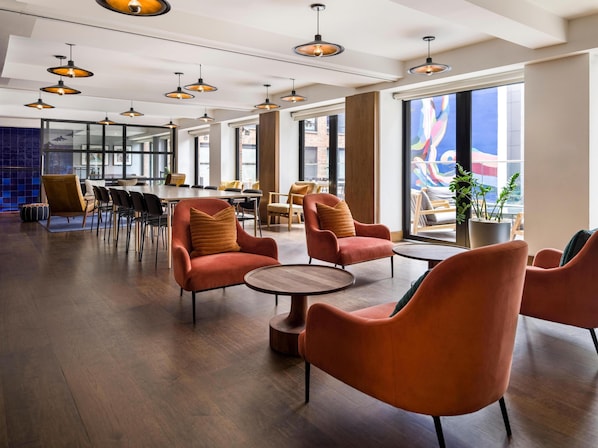 A spacious indoor area with multiple seating arrangements, including round tables and cushioned chairs, and large windows providing views of the outside. - Arlo SoHo (New York)