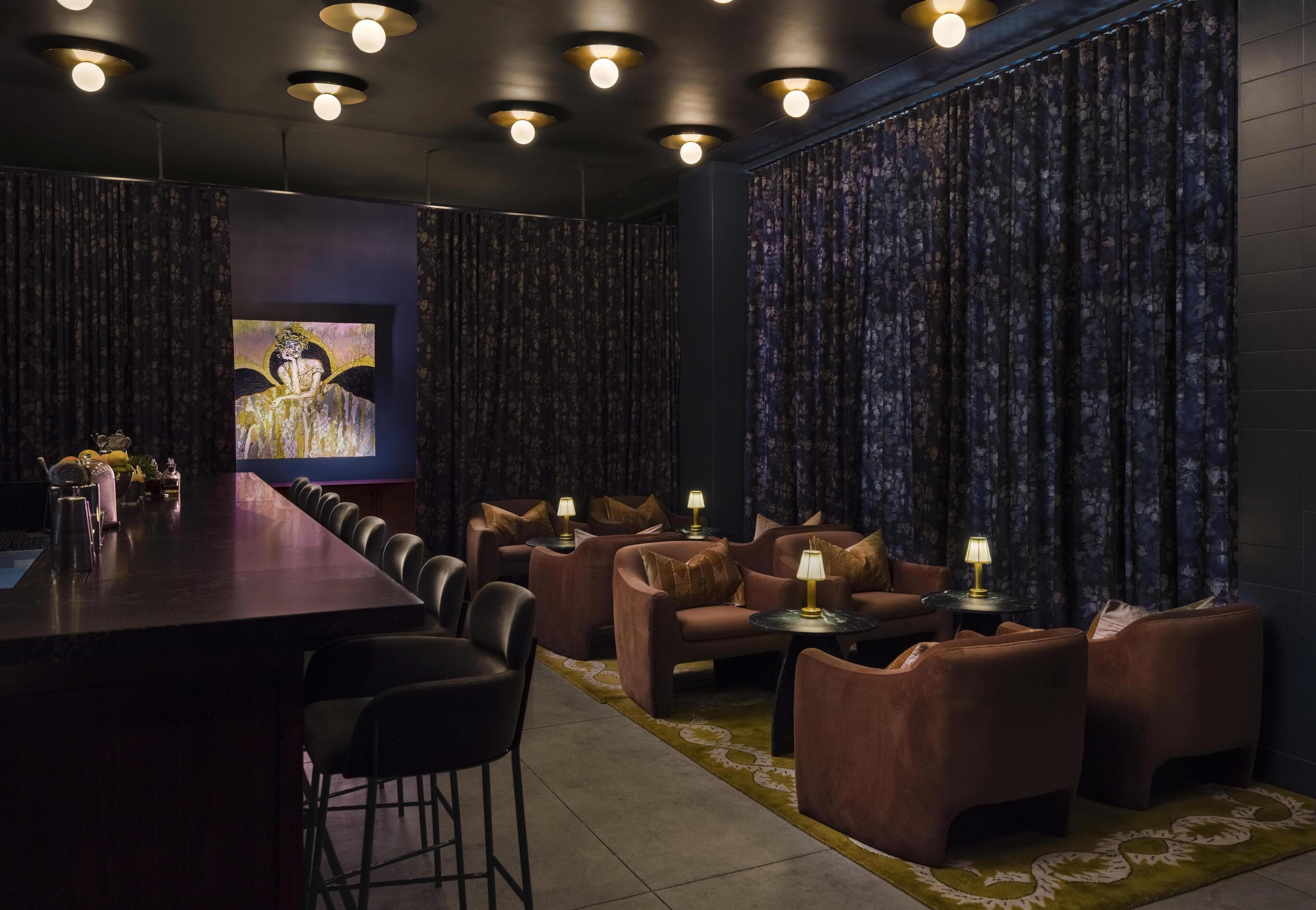 A room with a long table, several sofas, and chairs, with a painting on the wall and curtains on the windows.