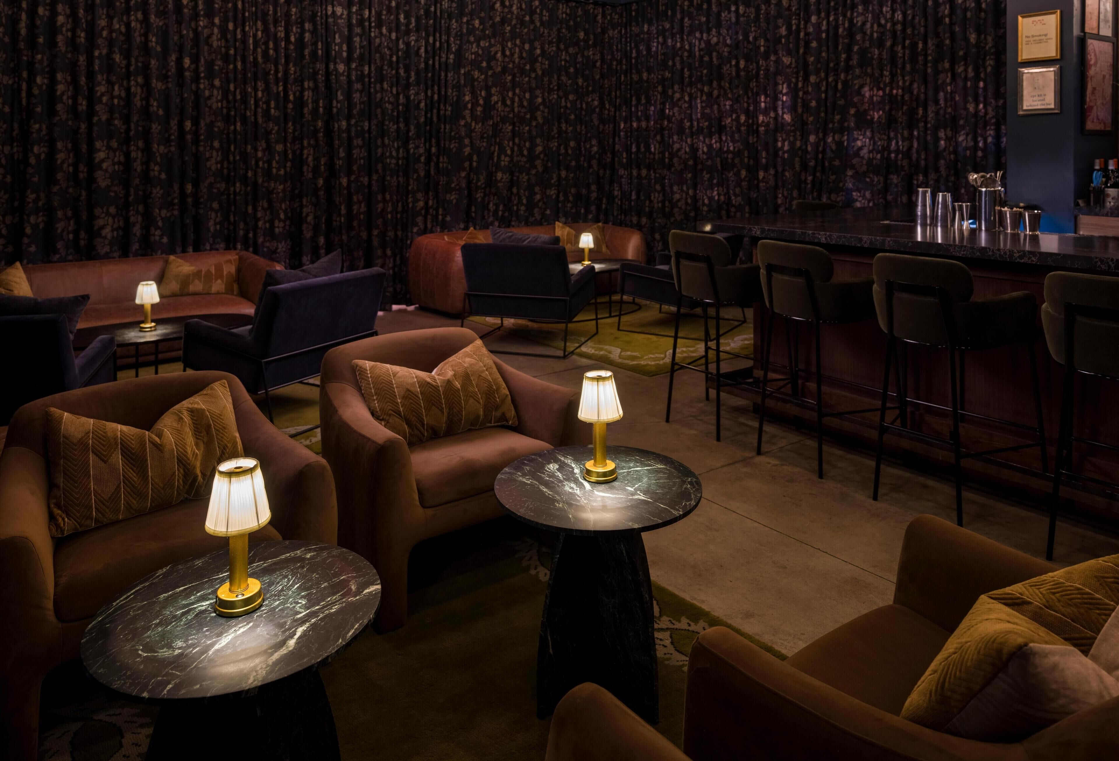 A cozy lounge area with sofas and armchairs, a bar counter, and a patterned wallpaper backdrop.