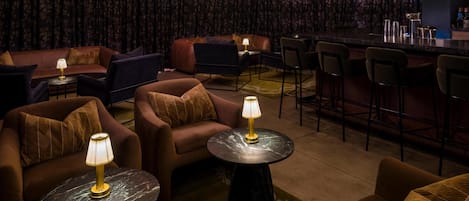 A cozy lounge area with sofas and armchairs, a bar counter, and a patterned wallpaper backdrop.