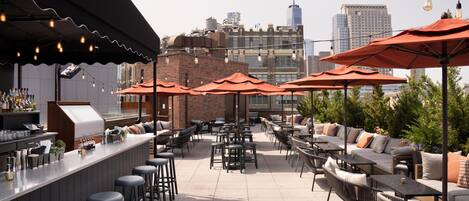 An outdoor patio with seating, a bar area, and city views.