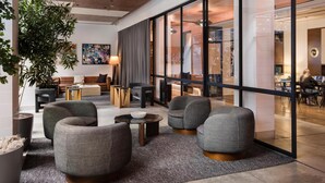 A modern lobby with grey upholstered seating, a large potted plant, and a large window offering a view of the interior. - Arlo SoHo (New York)