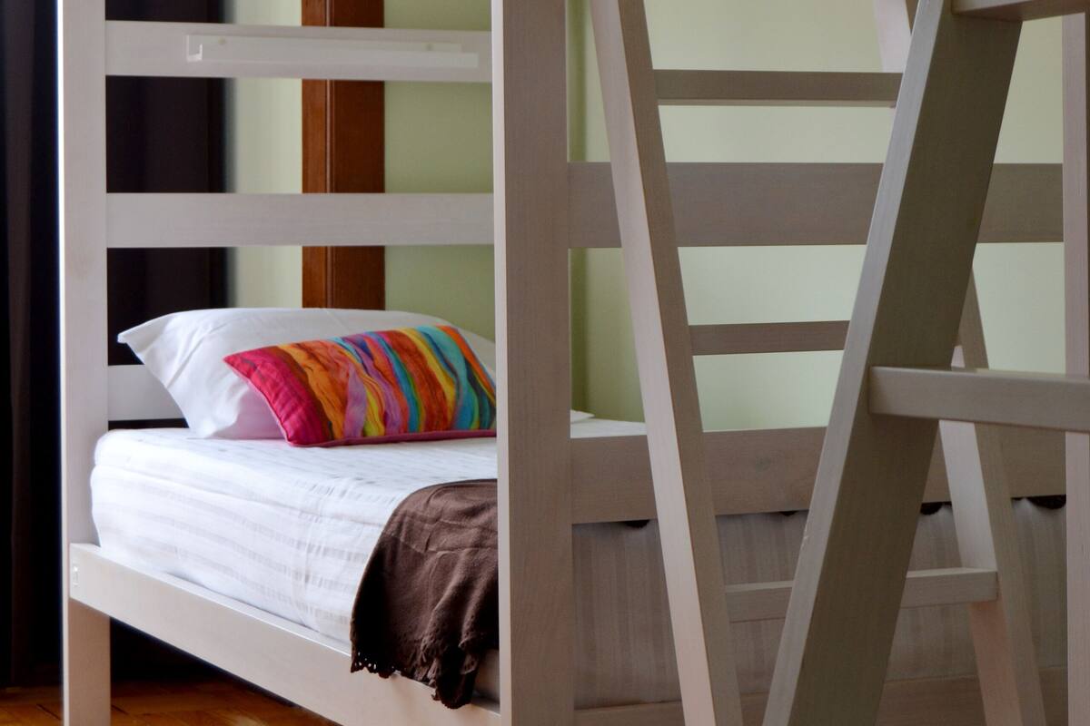 A bunk bed with a ladder, white bedding, and a colorful pillow.
