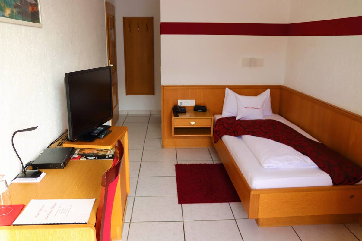 Ein Hotelzimmer mit einem Bett, einem Schreibtisch mit Fernseher, einem Nachttisch und einem roten Teppich.