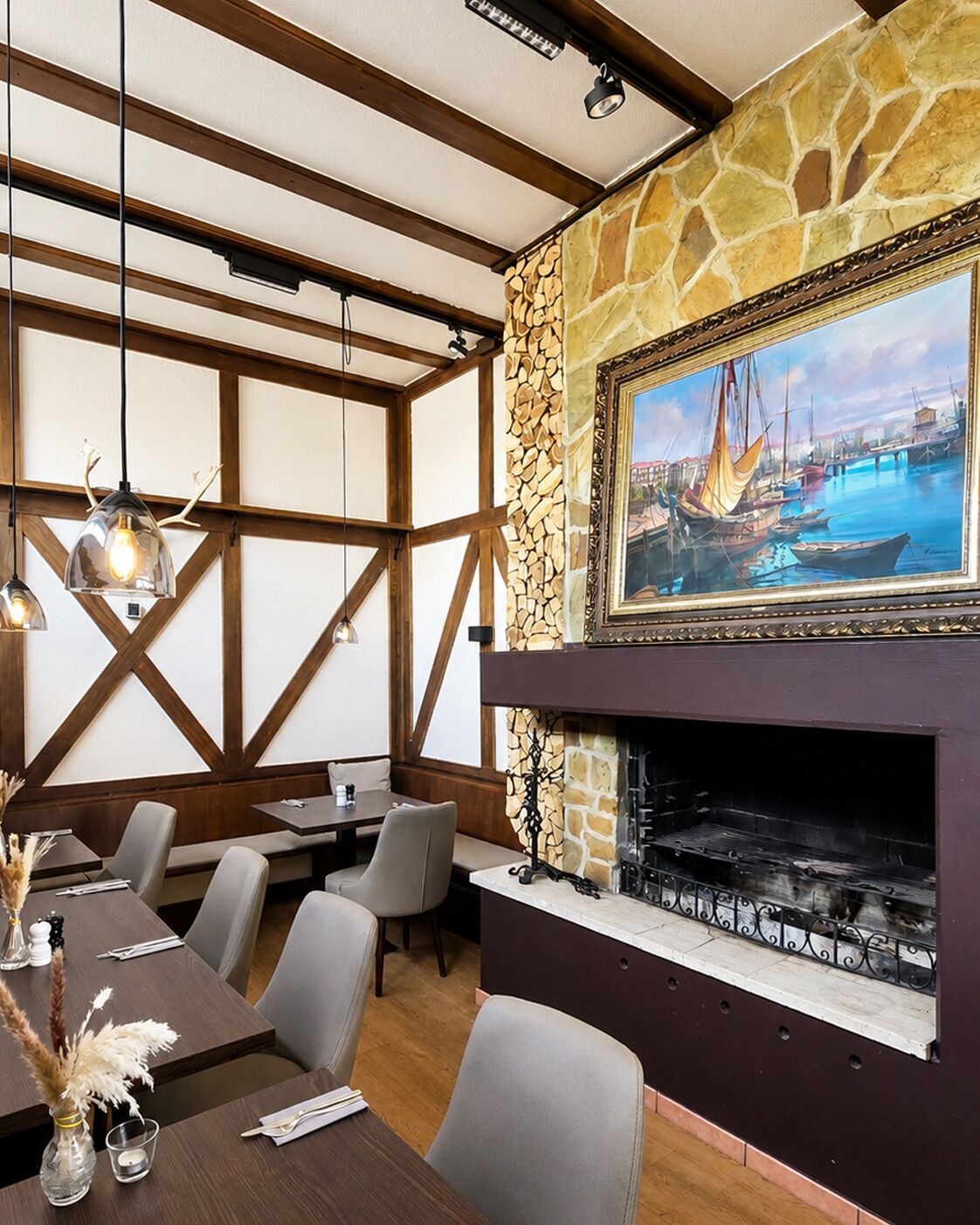 Een restaurantinterieur met houten balken, stenen muren, een open haard en een schilderij van een haven.