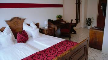 Una cama bien hecha con ropa de cama blanca y roja, un escritorio de madera con una lámpara y una silla.