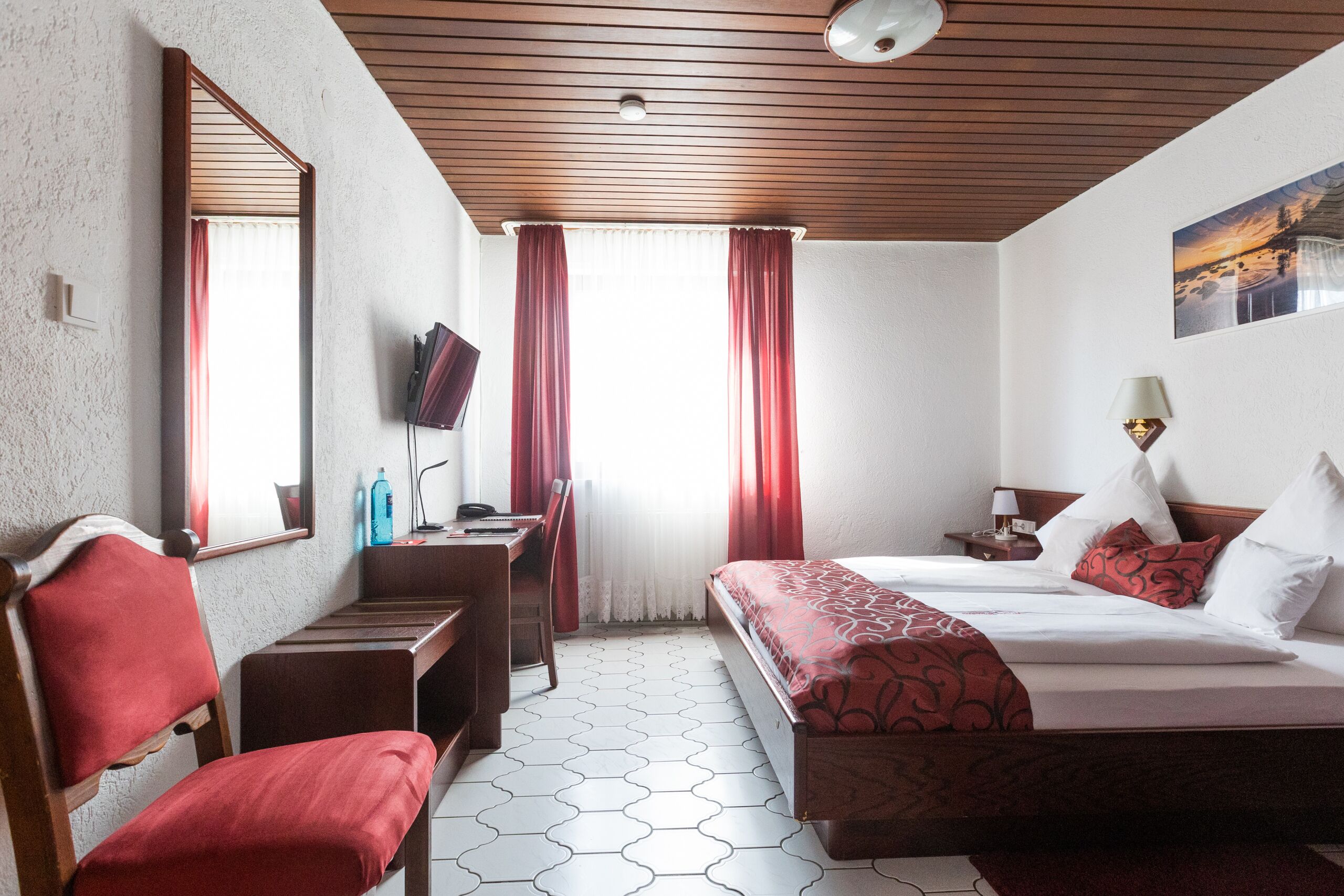 A hotel room with a bed, a desk, a chair, a TV, and a window with curtains.