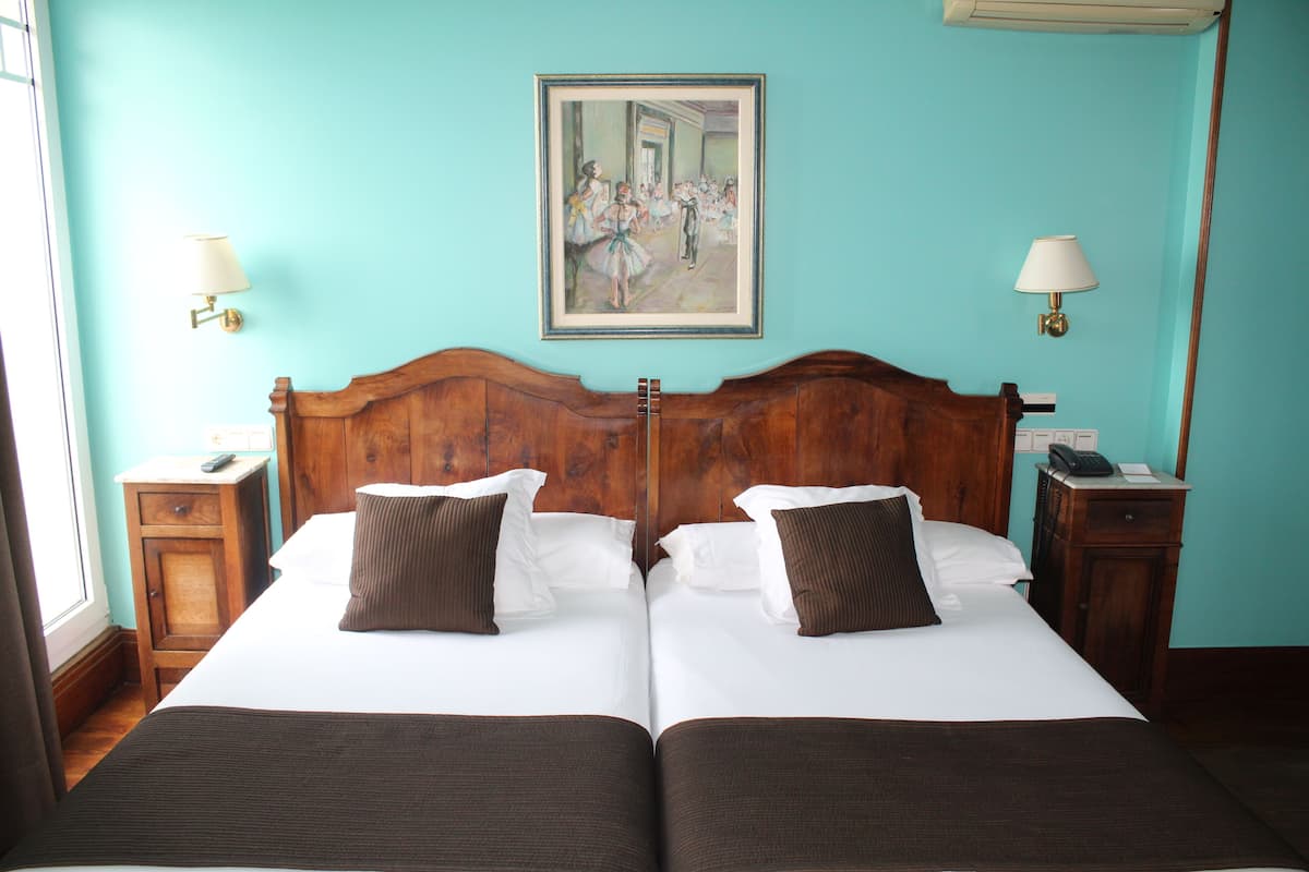 Ein Hotelzimmer mit zwei Betten, Holz-Kopfteilen, weißen Bettwäsche, braunen Kissen, einem Bild an der Wand und Nachttischlampen.