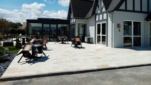 A modern building with a patio area featuring outdoor seating and a glass enclosure. - Hôtel le Pavillon de Rouen (Franqueville-Saint-Pierre)