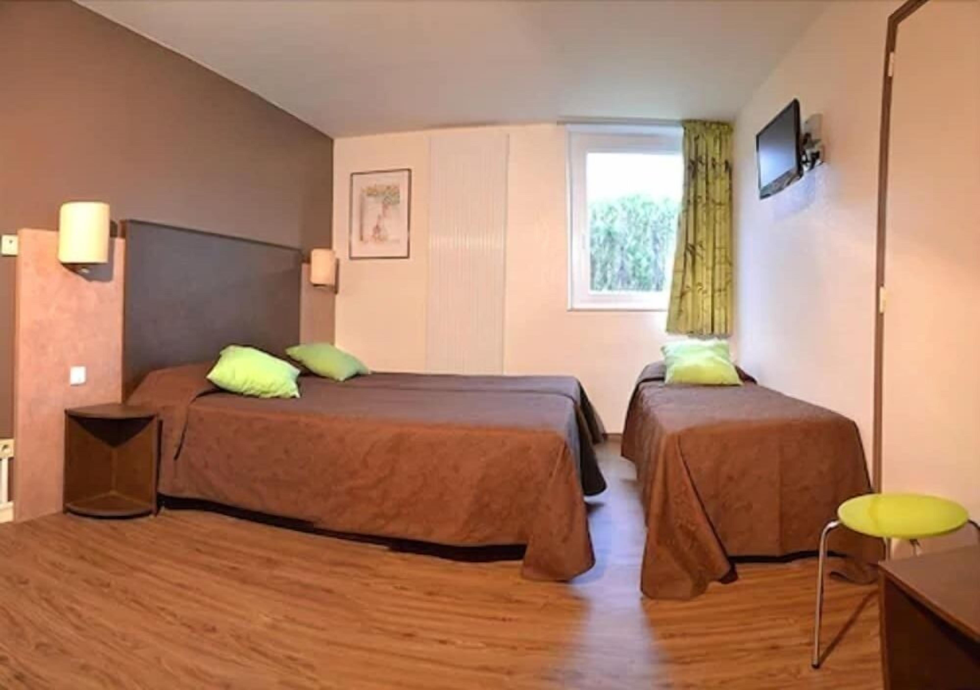 A room with two beds, a desk, a chair, a TV, and a window with curtains.