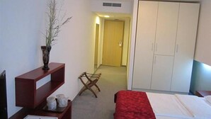 Una habitación de hotel con una cama, un escritorio con un florero y un bolígrafo, una silla y un armario.