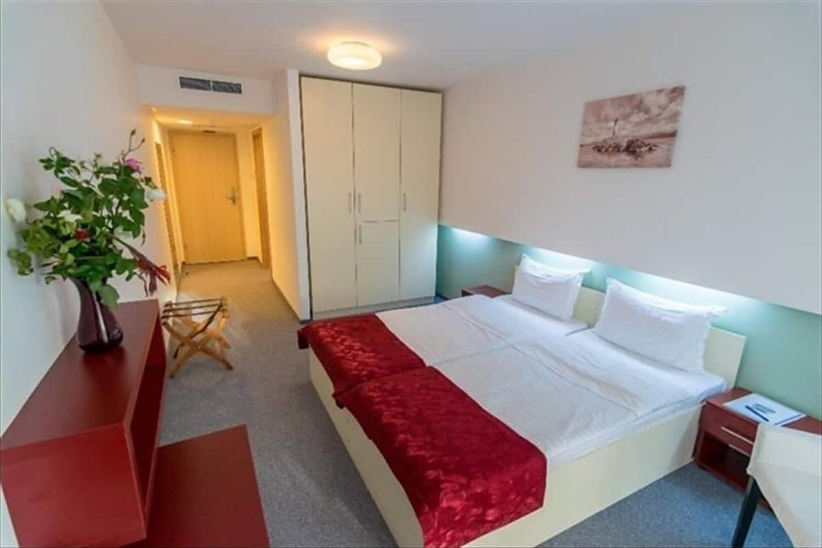 A hotel room with a bed, a nightstand, a desk, a chair, a wardrobe, and a painting on the wall.
