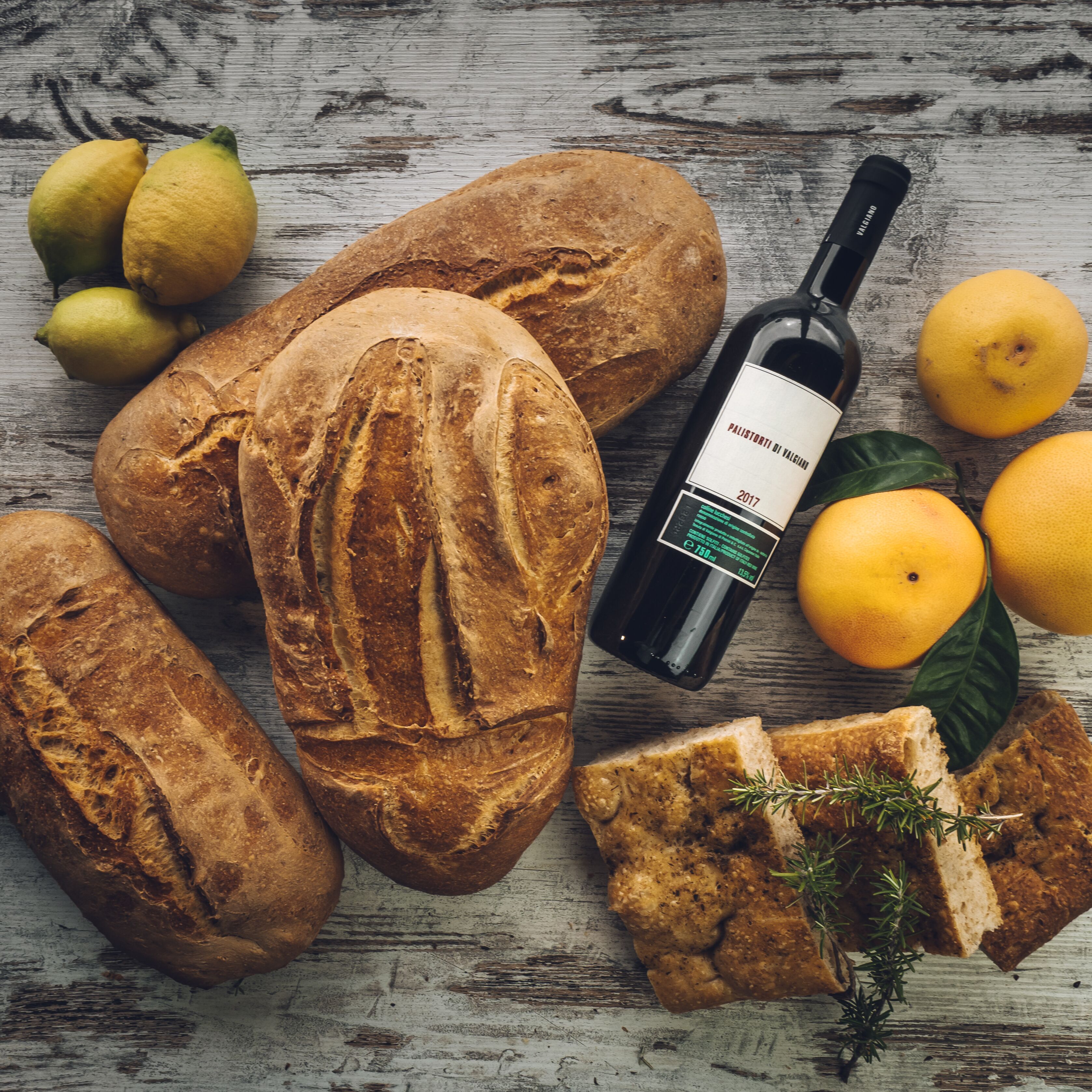 A rustic wooden table with various breads, lemons, and a bottle of wine.
