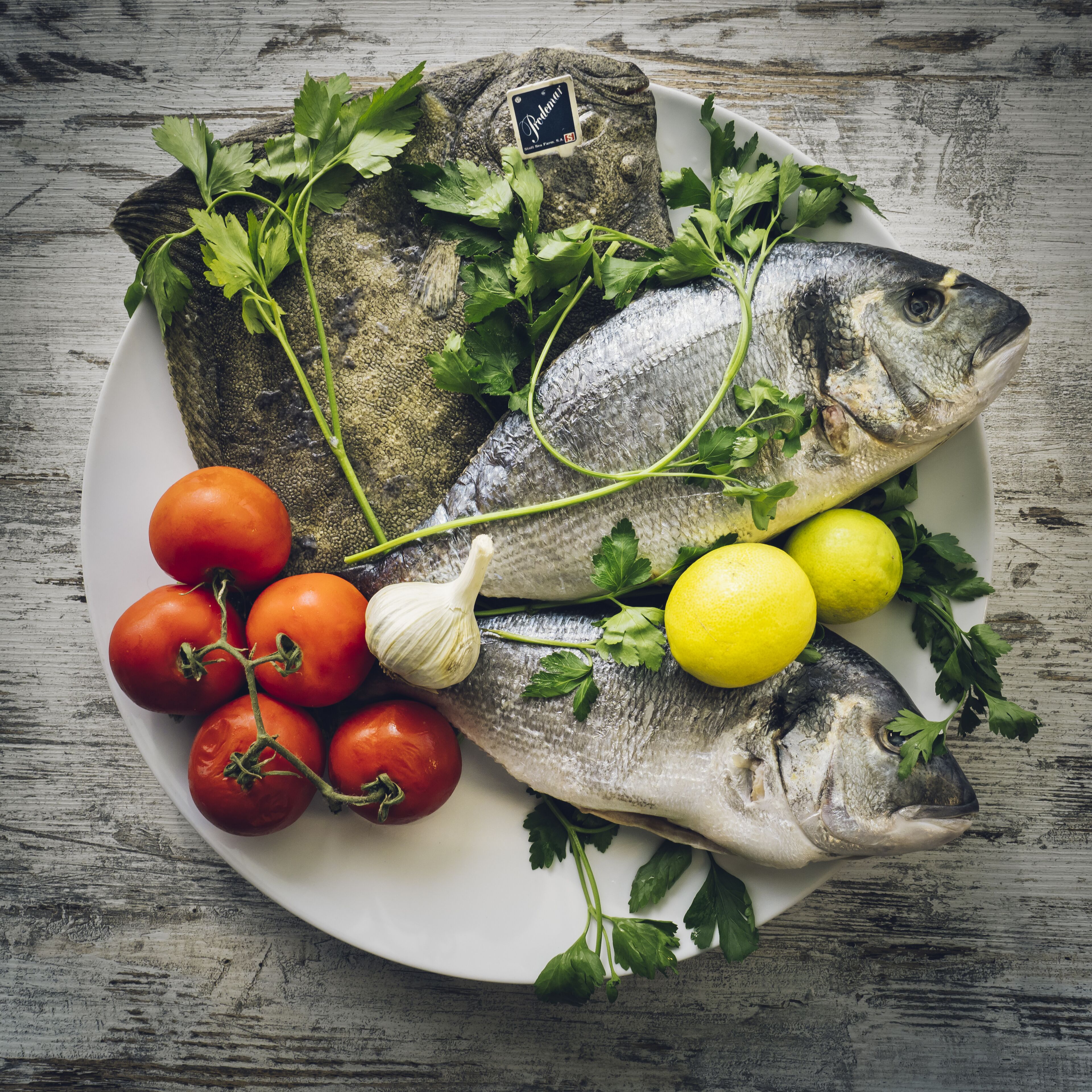 A plate with fish, tomatoes, parsley, and lemons.