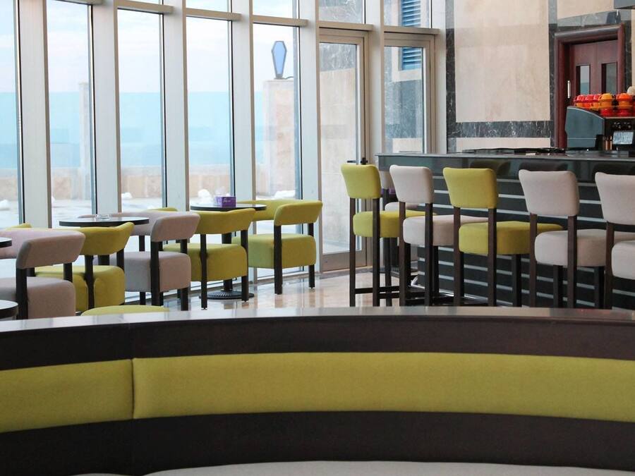 Un restaurante moderno con sillas amarillas y blancas, ventanas amplias y una zona de bar.