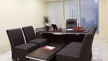 A conference room with a dark brown table, four black chairs, a laptop, a plant, and a window with blinds.