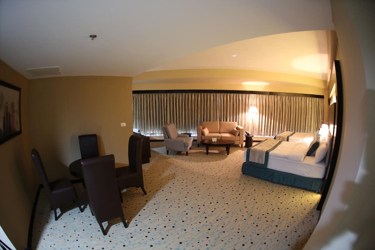 Une chambre d’hôtel avec un lit, un canapé, une chaise, une petite table et une fenêtre avec des rideaux.
