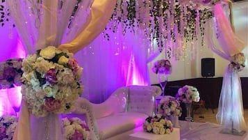 Bryllupsfest med hvid sofa, blomsterdekorationer og draperet stof.