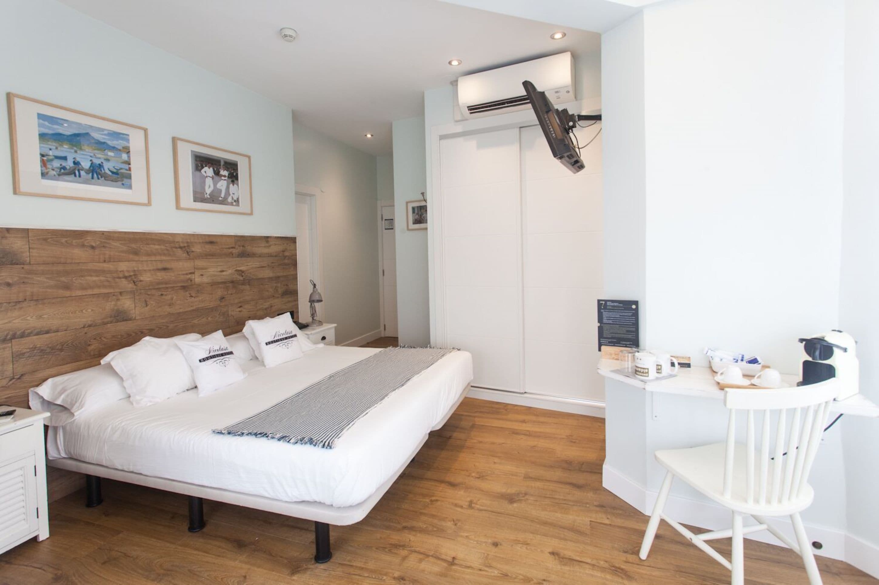 A modern bedroom with a wooden headboard, a large bed, a desk with a chair, and an air conditioning unit.
