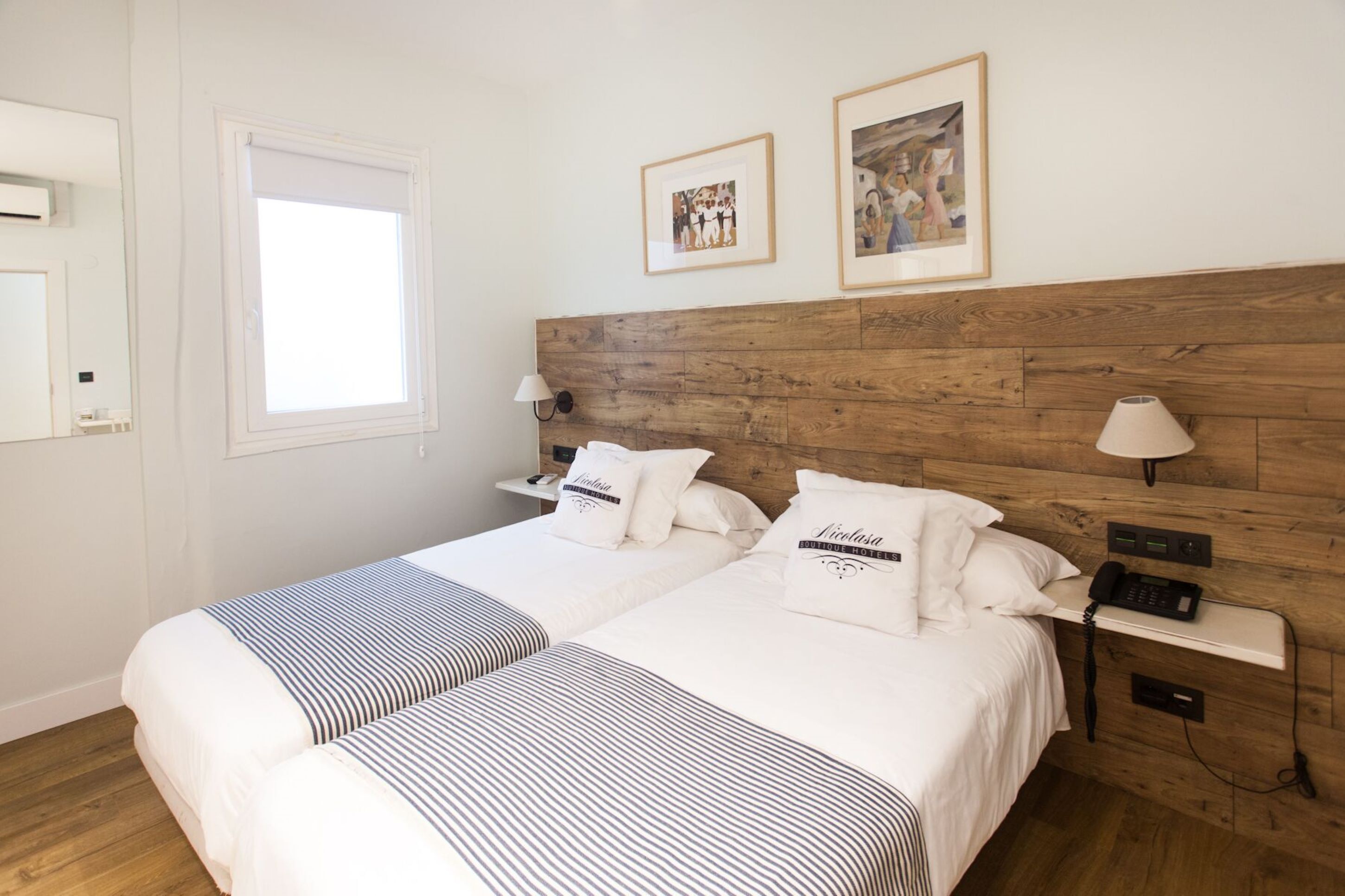 A double bed with a wooden headboard, two bedside tables with lamps, a window, and framed pictures on the wall.