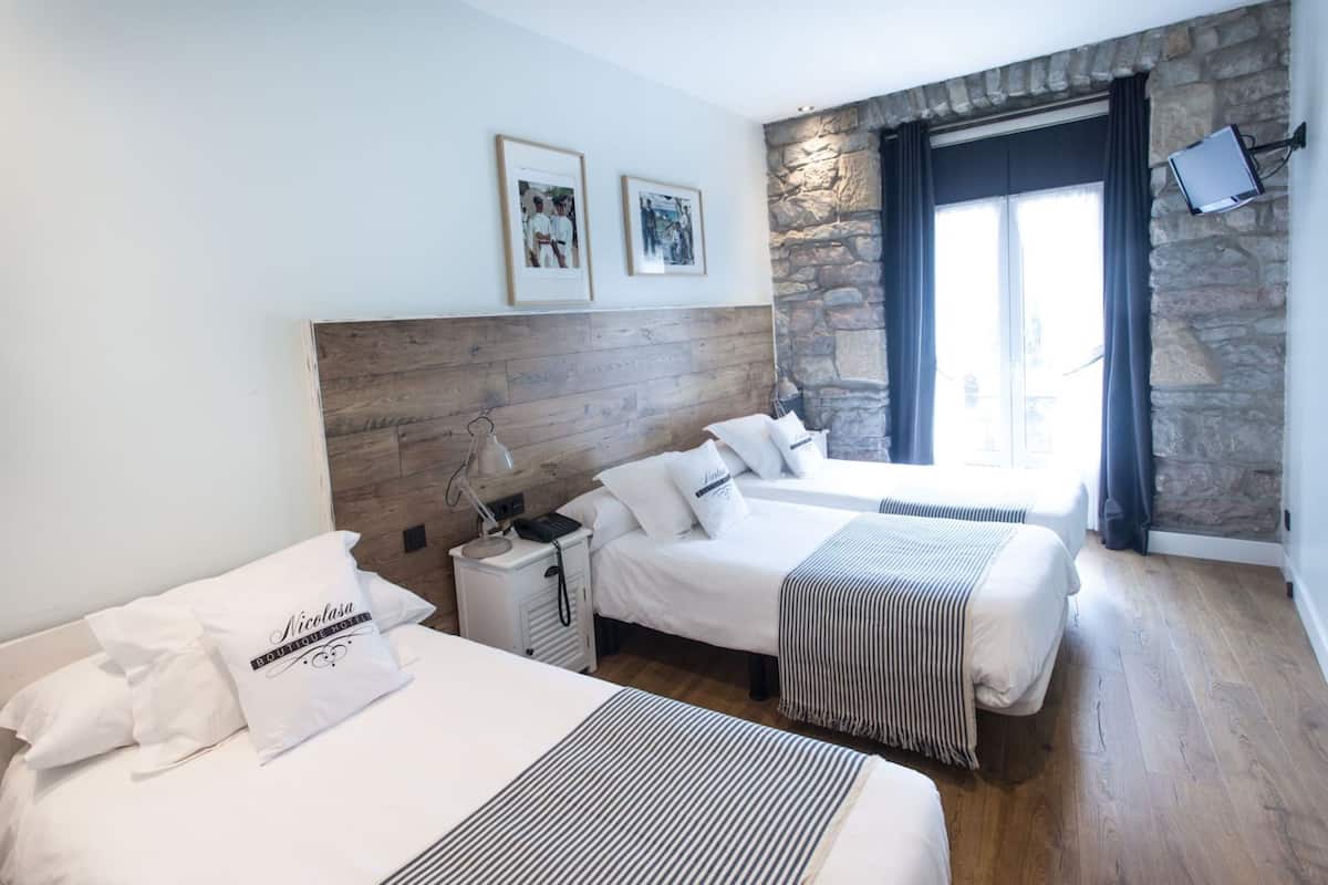 A hotel room with two beds, a stone accent wall, a mounted TV, and framed pictures on the wall.